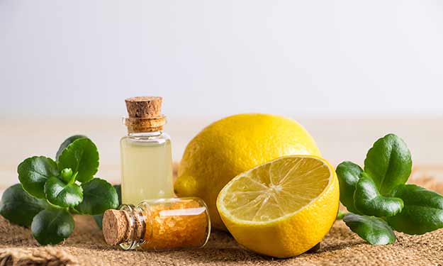 Un citron entier et demi se trouve sur une surface joliment décorée. Il y a aussi un petit verre dans lequel se trouve une huile essentielle.