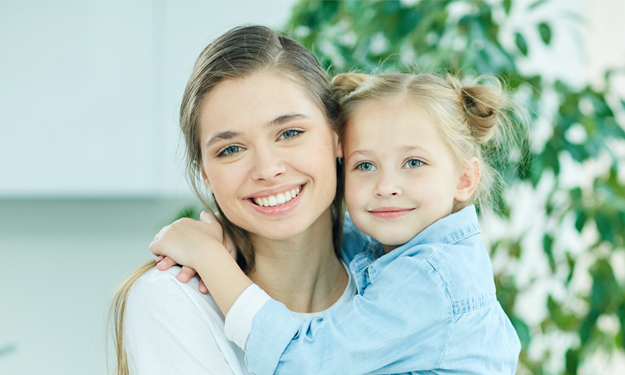Une jeune mère est assise dans une pièce lumineuse avec sa fille dans les mains et sourit au spectateur.